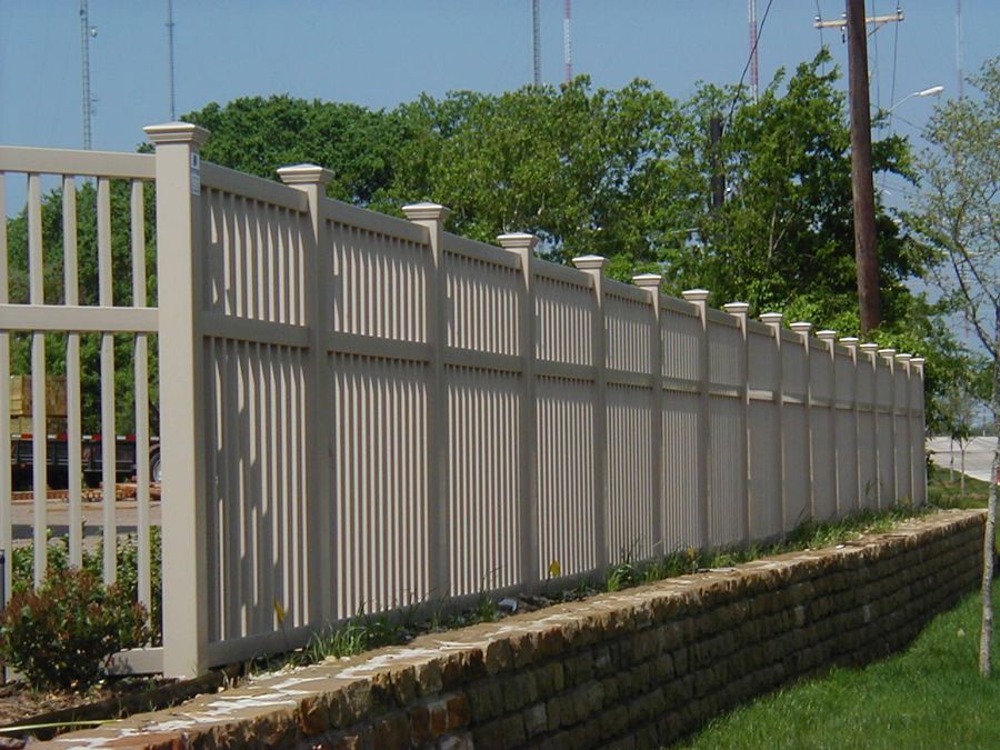 A white fence along a brick wall with trees in the background
