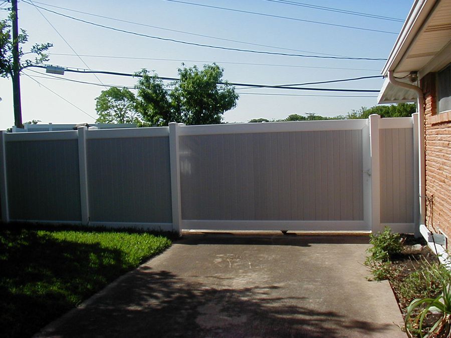 A gray and white fence surrounds a driveway leading to a house