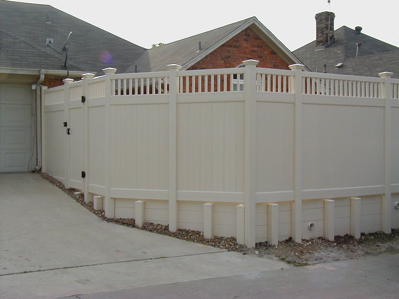 A white fence surrounds a driveway in front of a house