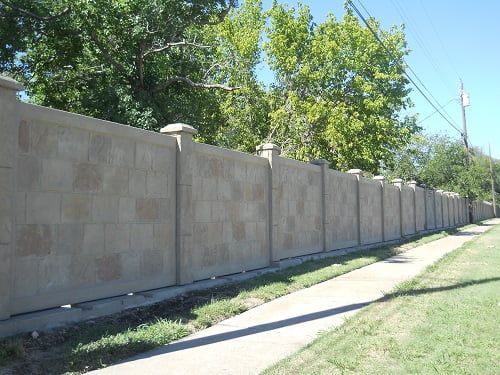 A brick fence along a sidewalk with trees in the background