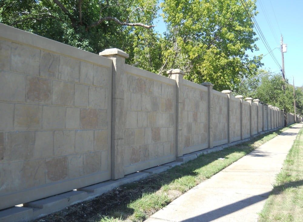A brick wall along a sidewalk with trees in the background