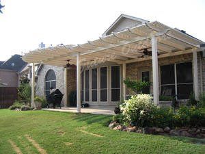 A white pergola is sitting on top of a lush green lawn in front of a house.