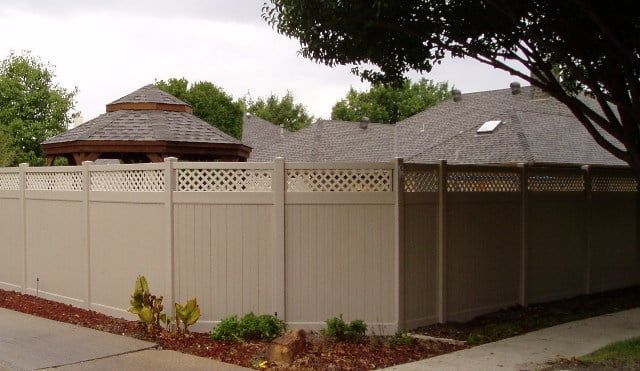 A white fence surrounds a house with a gazebo in the background