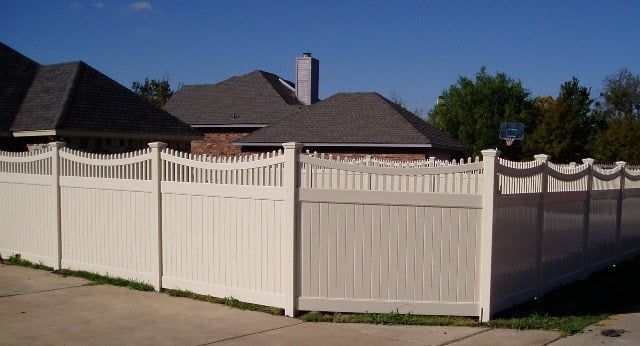 A white fence surrounds a driveway in front of a house.