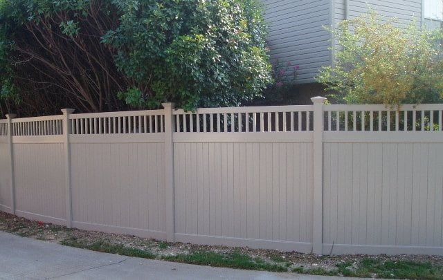 A white vinyl fence is sitting next to a sidewalk in front of a house.
