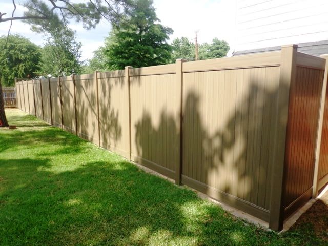 A wooden fence is surrounded by grass and trees in a backyard.