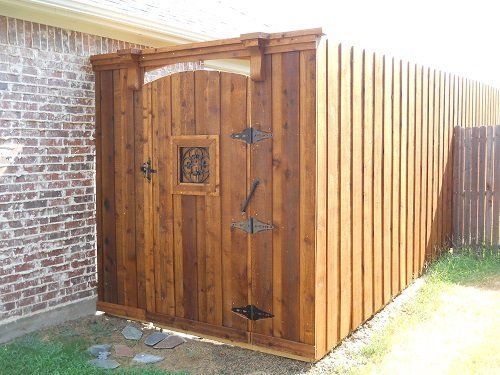A wooden shed with a wooden gate and a brick wall behind it.
