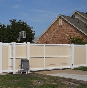 A white fence with a basketball hoop in the background is in front of a brick house.