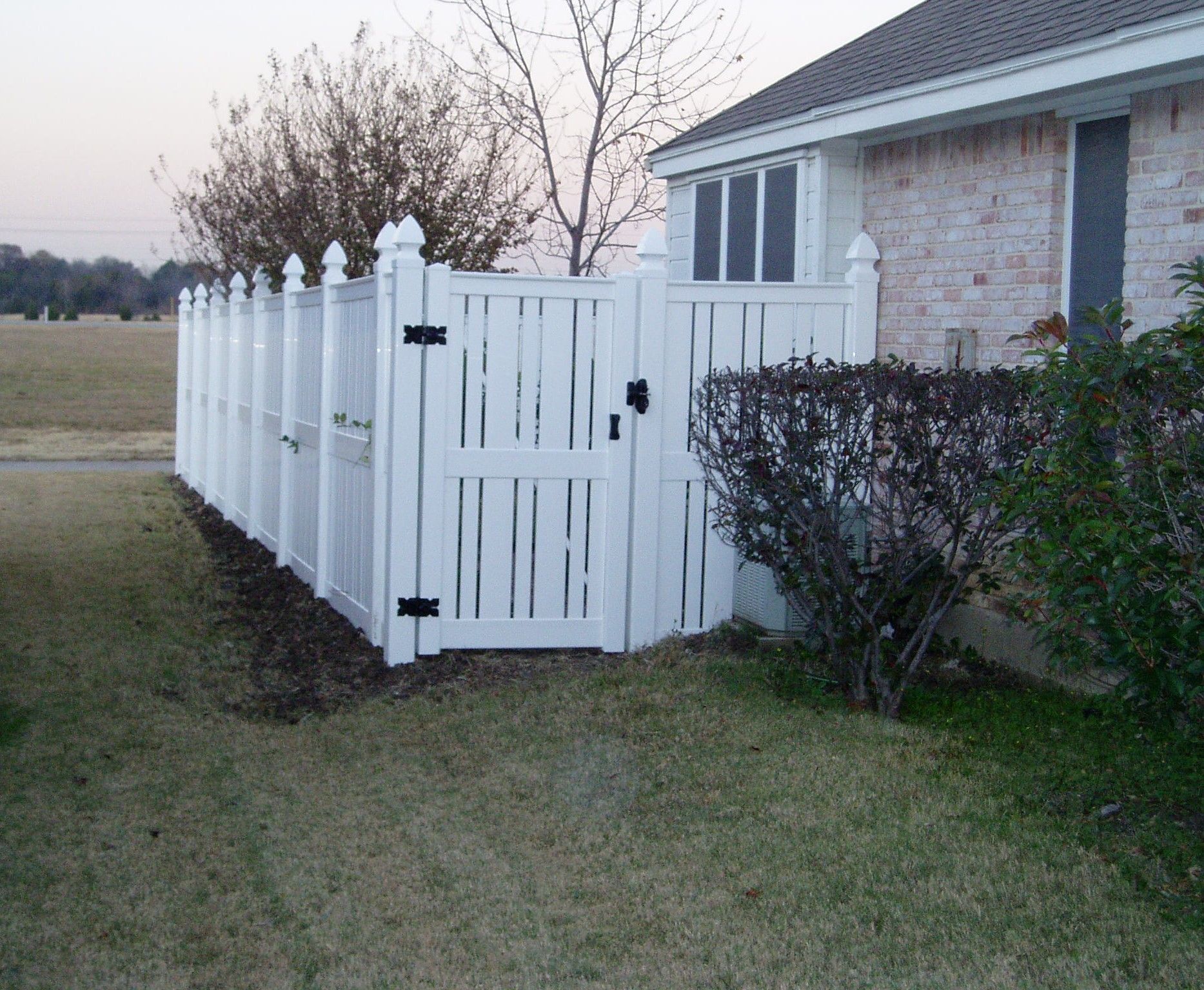 A white fence with a gate in front of a house.