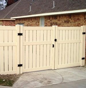 A white fence with a gate is in front of a brick house.