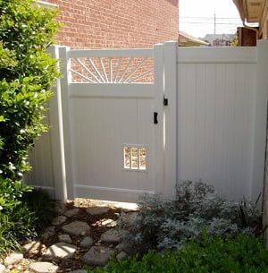 A white fence with a gate and a brick wall in the background.
