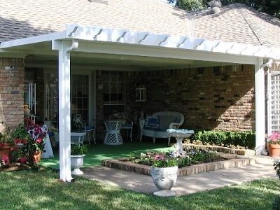 A patio with a white pergola and a brick house in the background