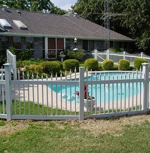 A white fence surrounds a swimming pool in front of a house.