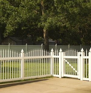 A white fence with a gate is surrounded by grass and trees.