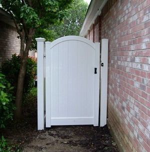A white gate is sitting next to a brick wall.