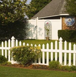 A white picket fence surrounds a lush green yard in front of a house.