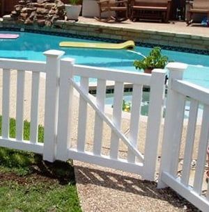 A white fence is surrounding a swimming pool.