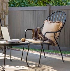 A chair with a pillow on it is sitting on a porch next to a table with a laptop on it.