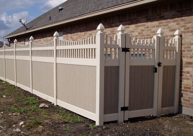 A white fence with a gate in front of a brick building.