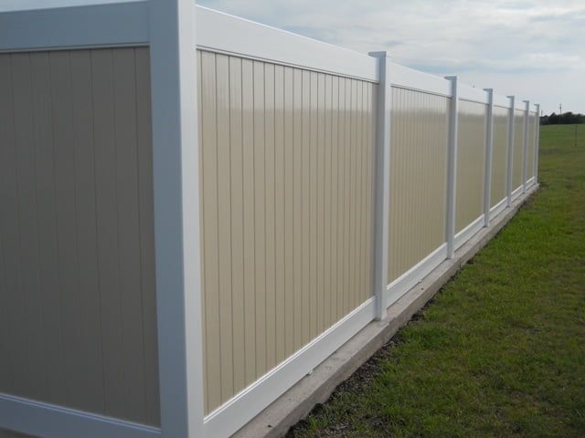 A white and tan fence is sitting in the middle of a grassy field.