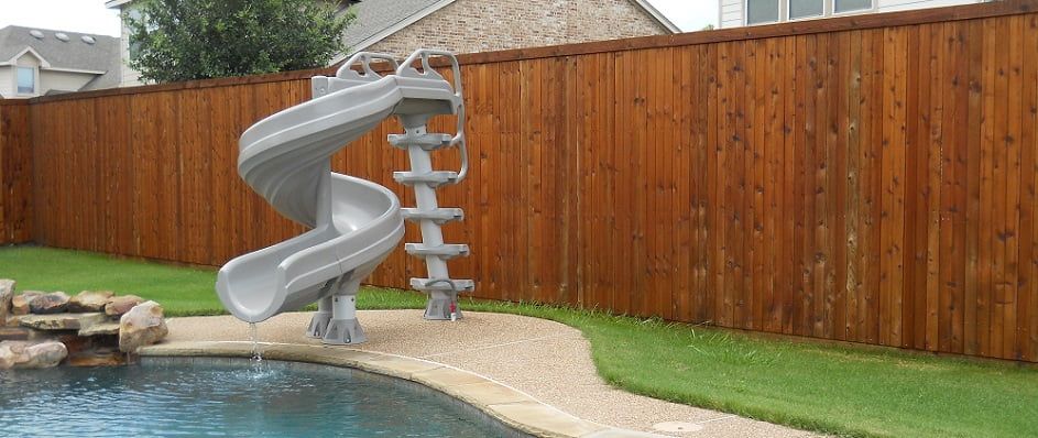 A pool with a slide attached to it and a wooden fence.