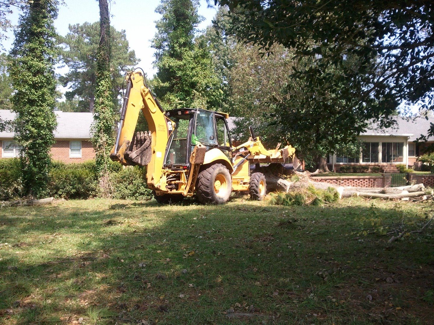 a yellow backhoe is parked in the grass in front of a house