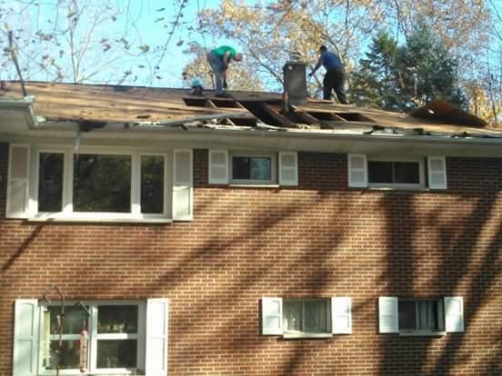 Two men are working on the roof of a brick house
