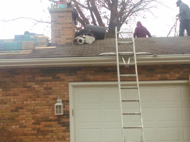 A man is standing on the roof of a house with a ladder.