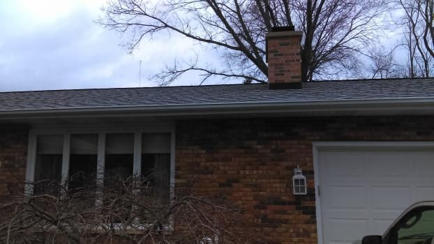 A car is parked in front of a brick house with a chimney on the roof.