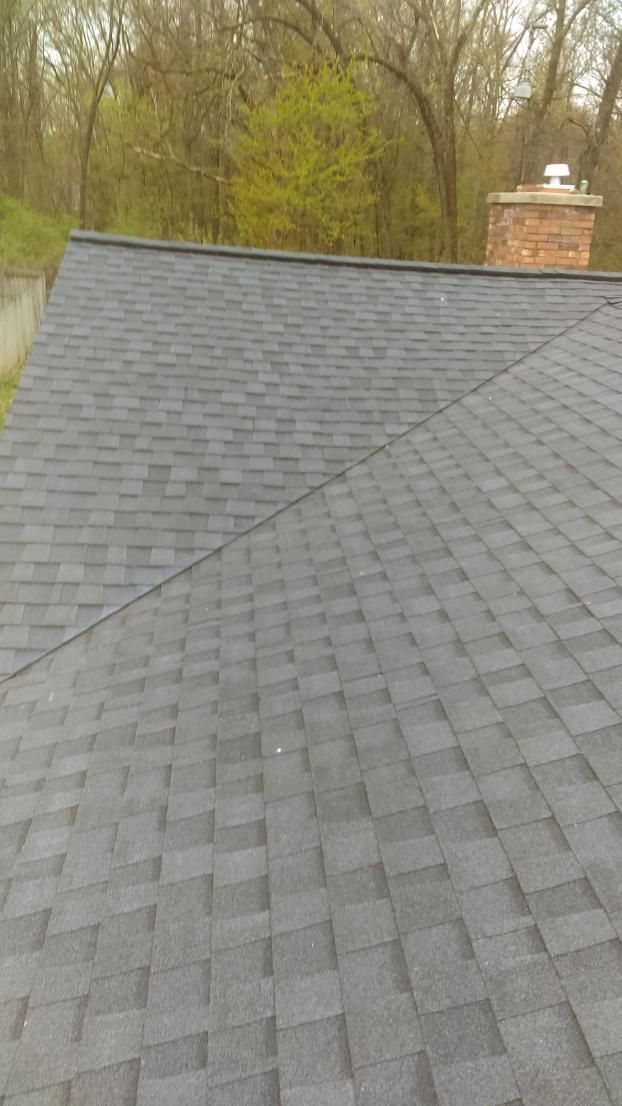 A close up of a roof with a chimney and trees in the background.