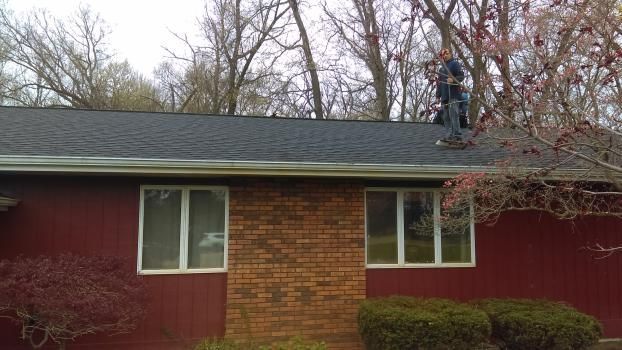 A man is working on the roof of a red house.
