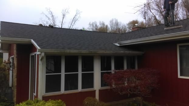 A man is standing on the roof of a red house.