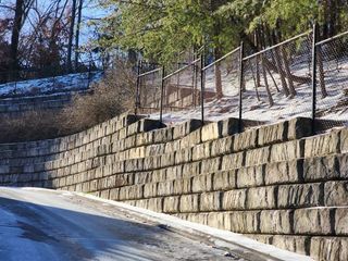 A stone wall along the side of a road next to a chain link fence.