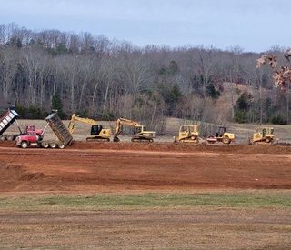 A row of construction vehicles are working on a dirt field.