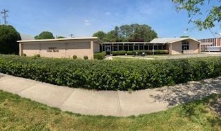 Low building with large windows and a green hedge in front on a sunny day.
