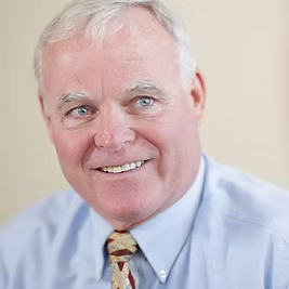 A man in a blue shirt and tie is smiling for the camera.