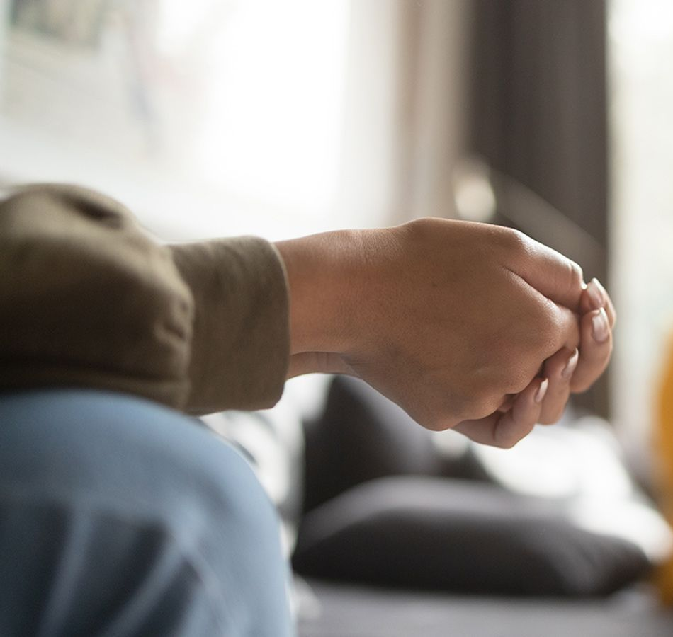Two people seated, gently holding hands indoors, one in a mint sweater and gray pants.