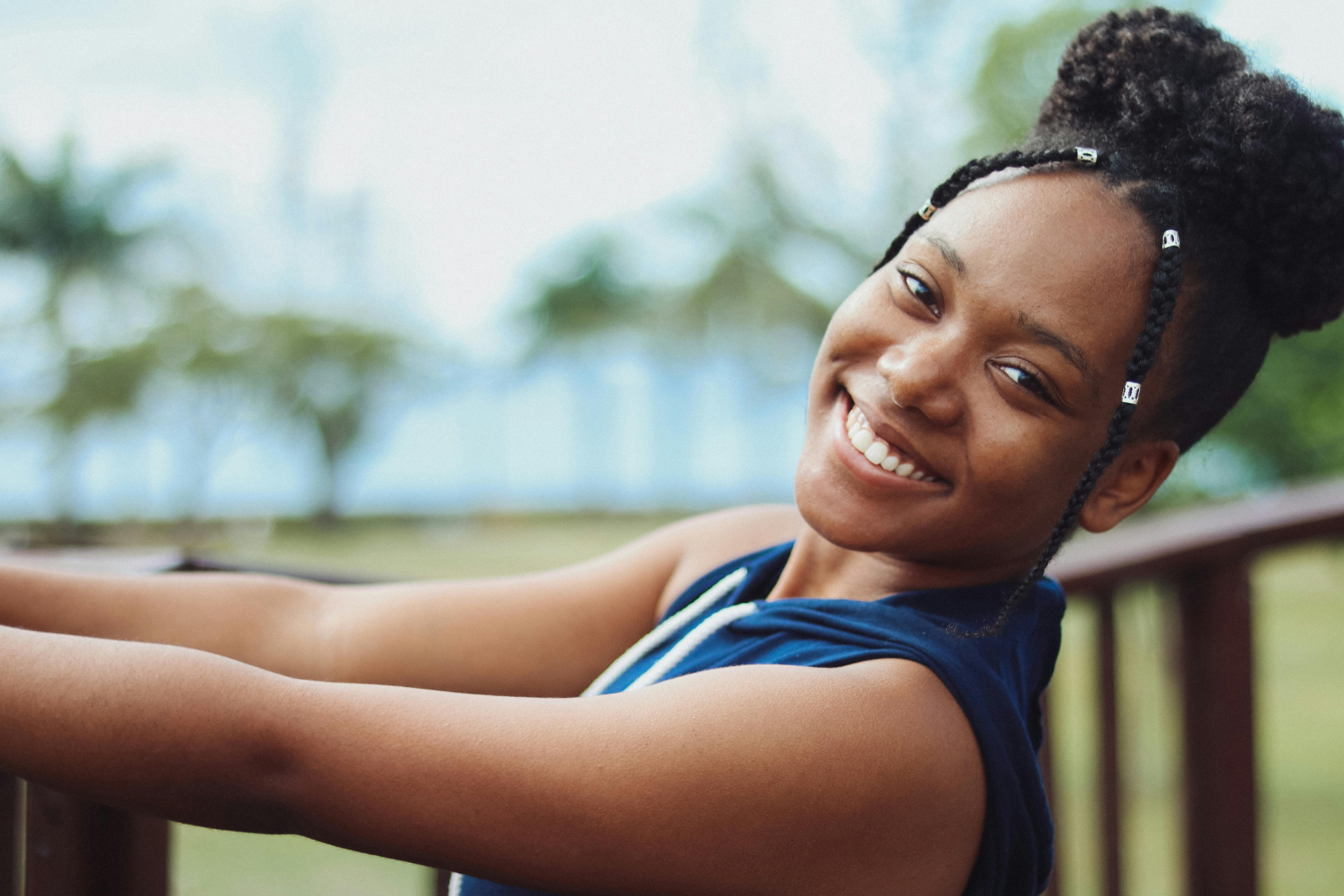 Smiling woman in a blue top leaning on a railing outdoors with blurred trees in the background