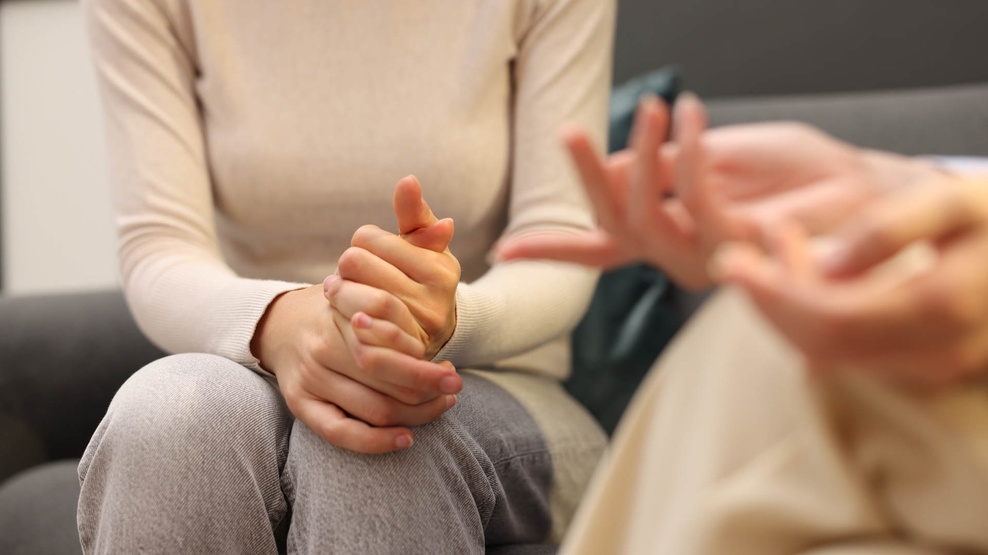 Two people seated in conversation, one holding the other's hand in a supportive gesture.