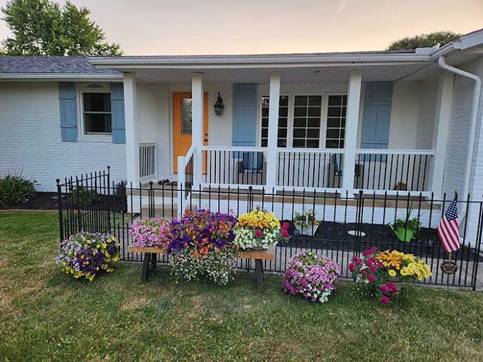 A white house with a porch and flowers in front of it.