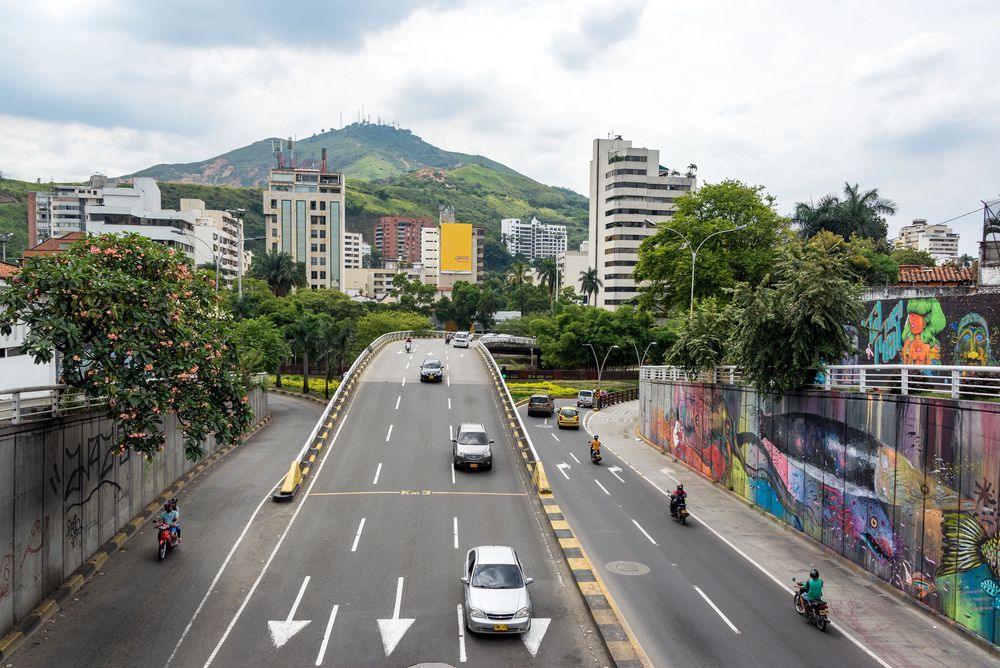 Carretera ancha con tráfico en una ciudad; edificios y una montaña al fondo.
