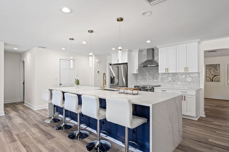 Modern kitchen with white cabinets, island seating, stainless hood, and wood-look flooring
