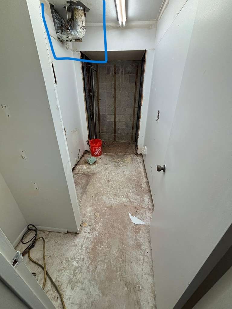 Narrow hallway with a ceiling vent, unfinished floors, and a door on the right.