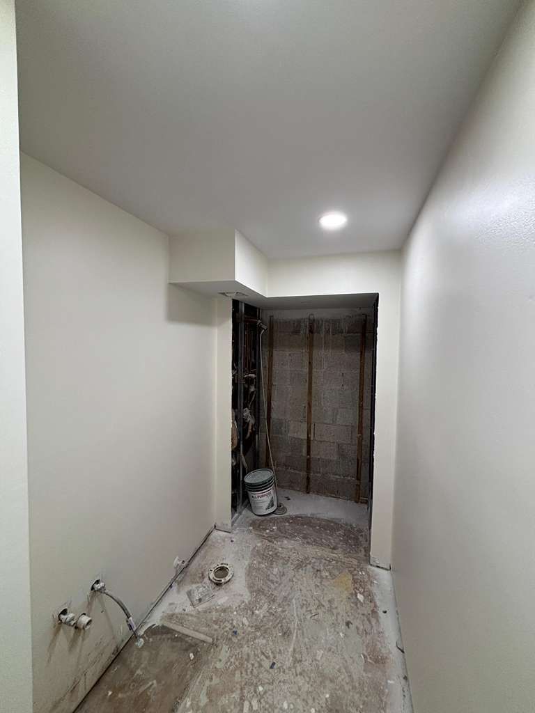 A narrow hallway with a paint bucket and washer dryer connections coming out of the wall