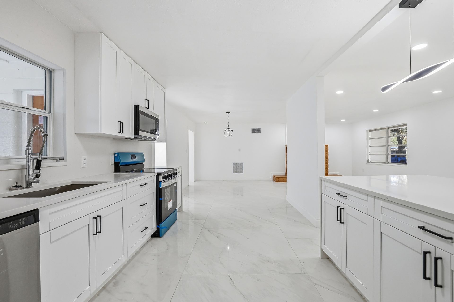 Bright white kitchen with cabinetry, stainless steel appliances, and island with pendant lights.
