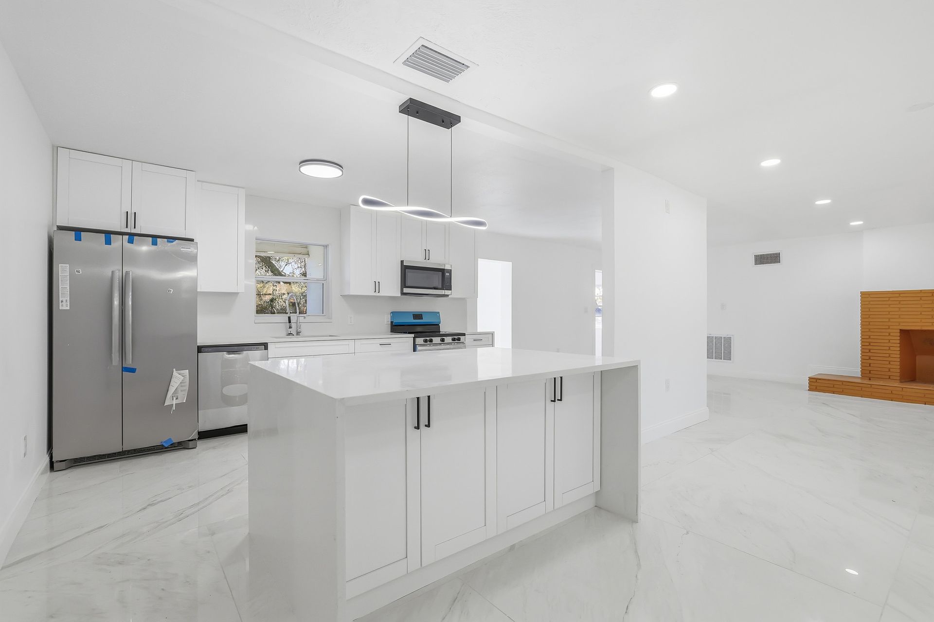 Modern white kitchen with island, stainless steel appliances, and tiled floors.