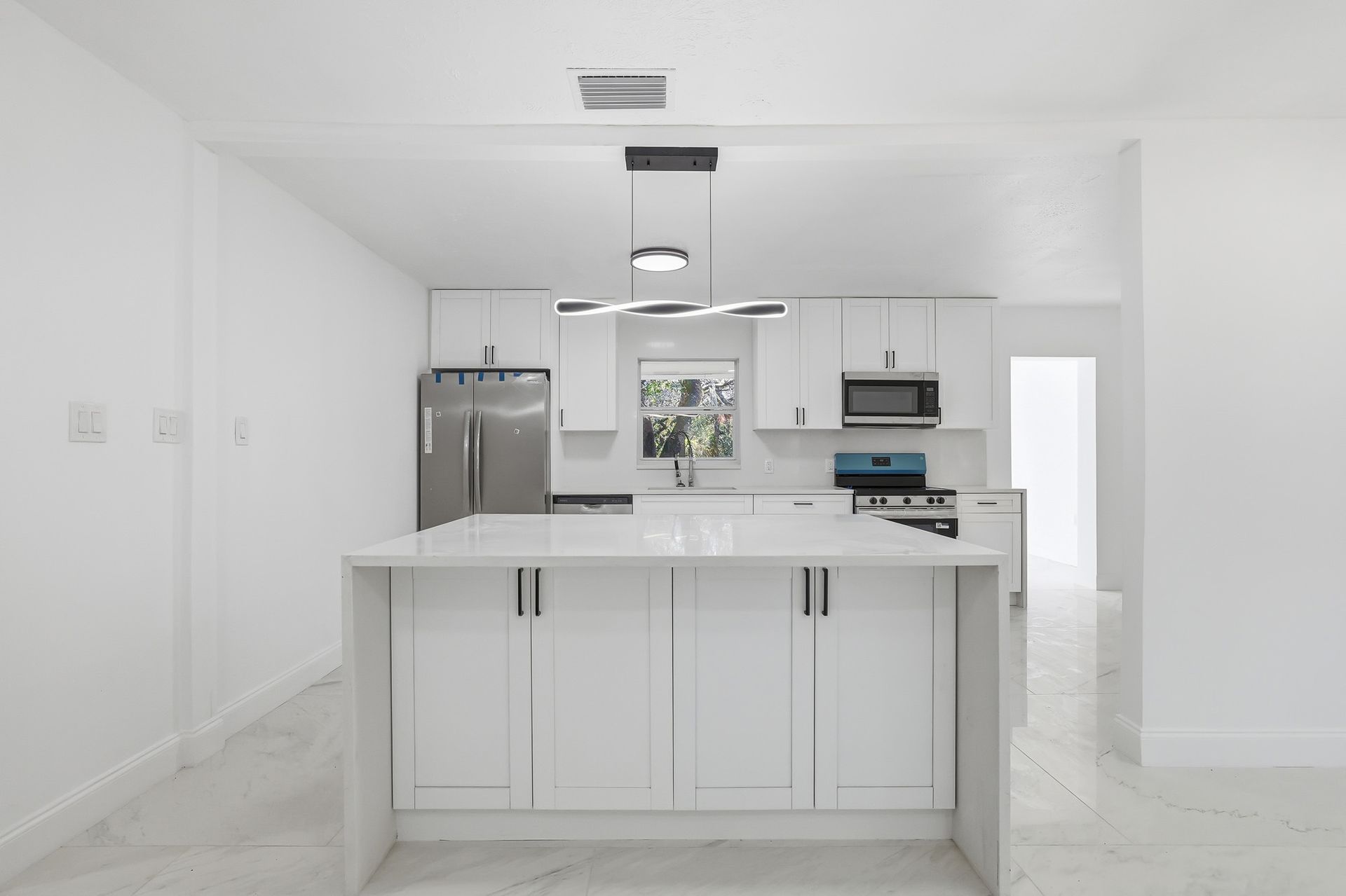 White kitchen with island, stainless steel appliances, and modern lighting.