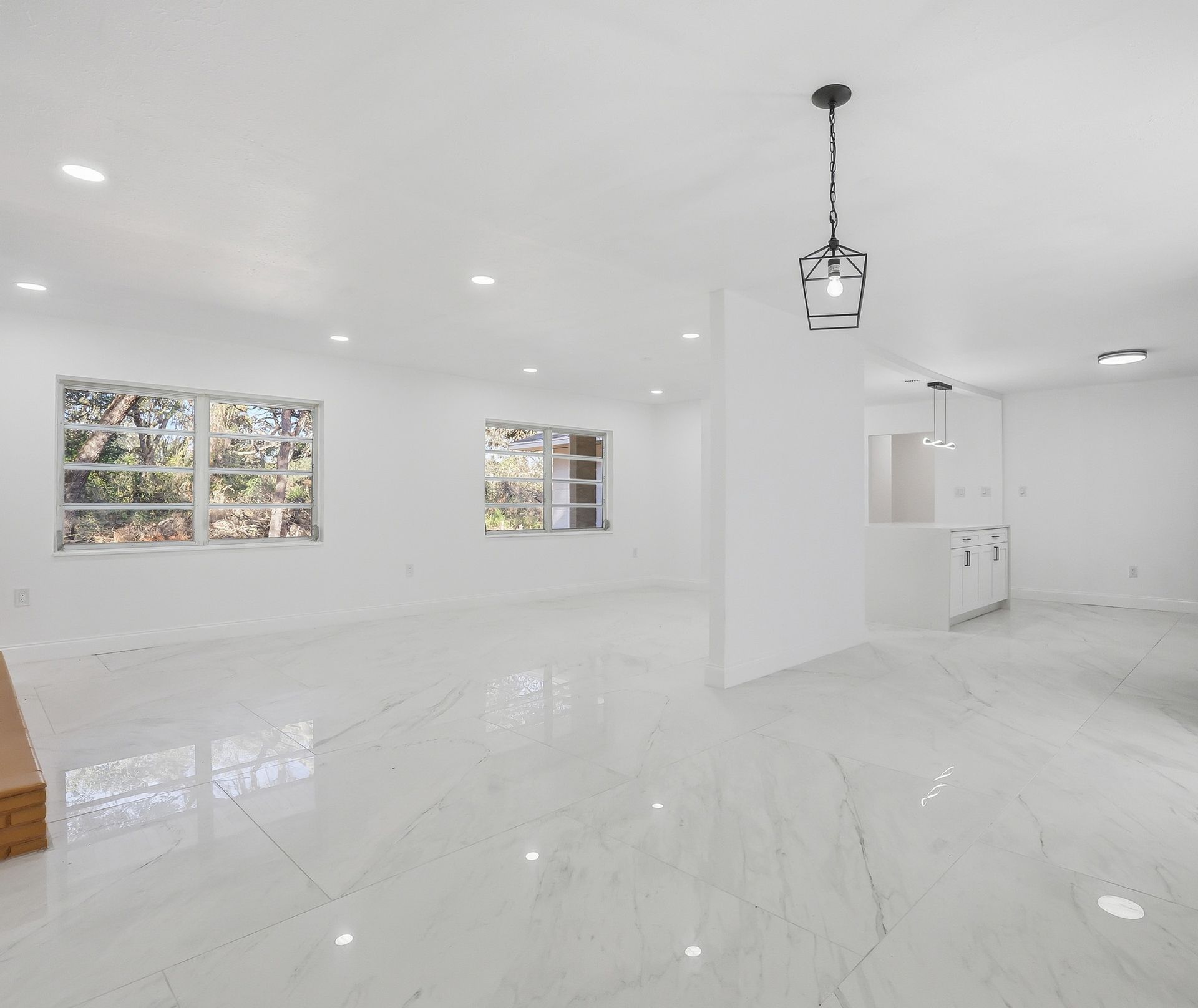 Spacious, white-walled room with large windows, marble-like floor, and a hanging light fixture.