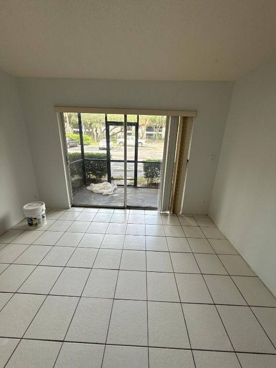 Empty room with white tile floor, sliding glass door to outside, paint bucket, and vertical blinds.