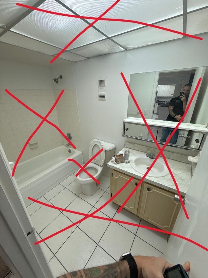Bathroom with a tub, toilet, vanity, and a person reflected in the mirror, with red lines overlaid.